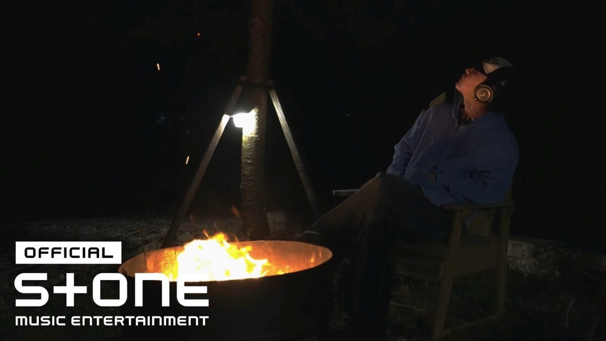 Homem sentado em cadeira, ouvindo música, olhando para o céu sob a luz de uma fogueira à noite.