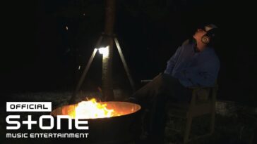 Homem sentado em cadeira, ouvindo música, olhando para o céu sob a luz de uma fogueira à noite.