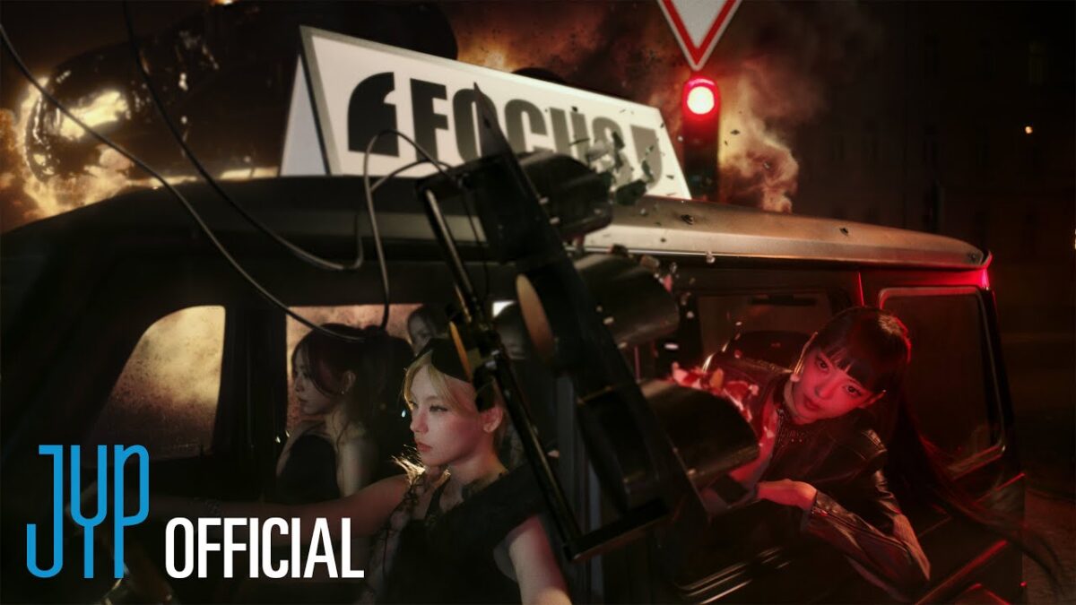Três integrantes do ITZY em um carro, com luzes vermelhas e uma atmosfera de ação ao fundo.