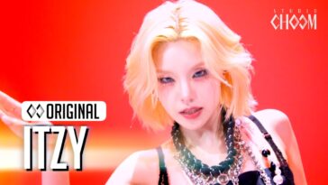 Membro do ITZY exibe look impactante em performance vibrante com fundo vermelho e acessórios chamativos.