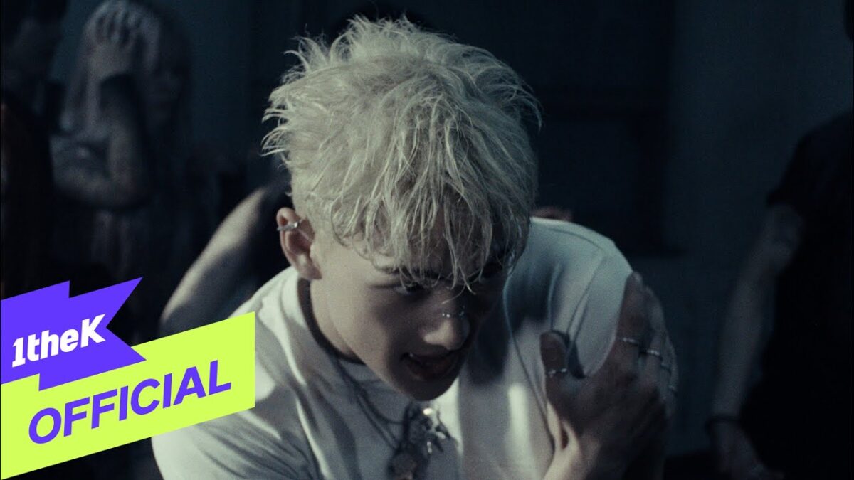 Baekho com cabelo platinado e piercings, expressando intensidade em um cenário escuro e dramático.