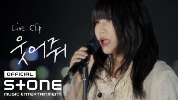 Cantora em performance ao vivo, segurando um microfone, com luzes desfocadas ao fundo.