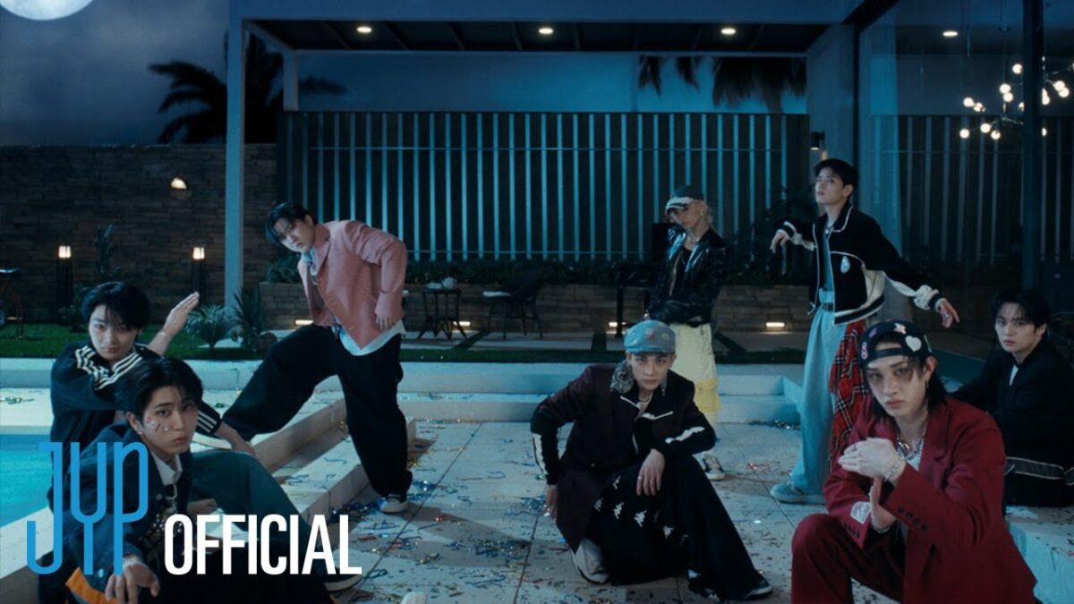 Sete membros do Stray Kids posam em um ambiente noturno, cercados por luzes e decoração vibrante.