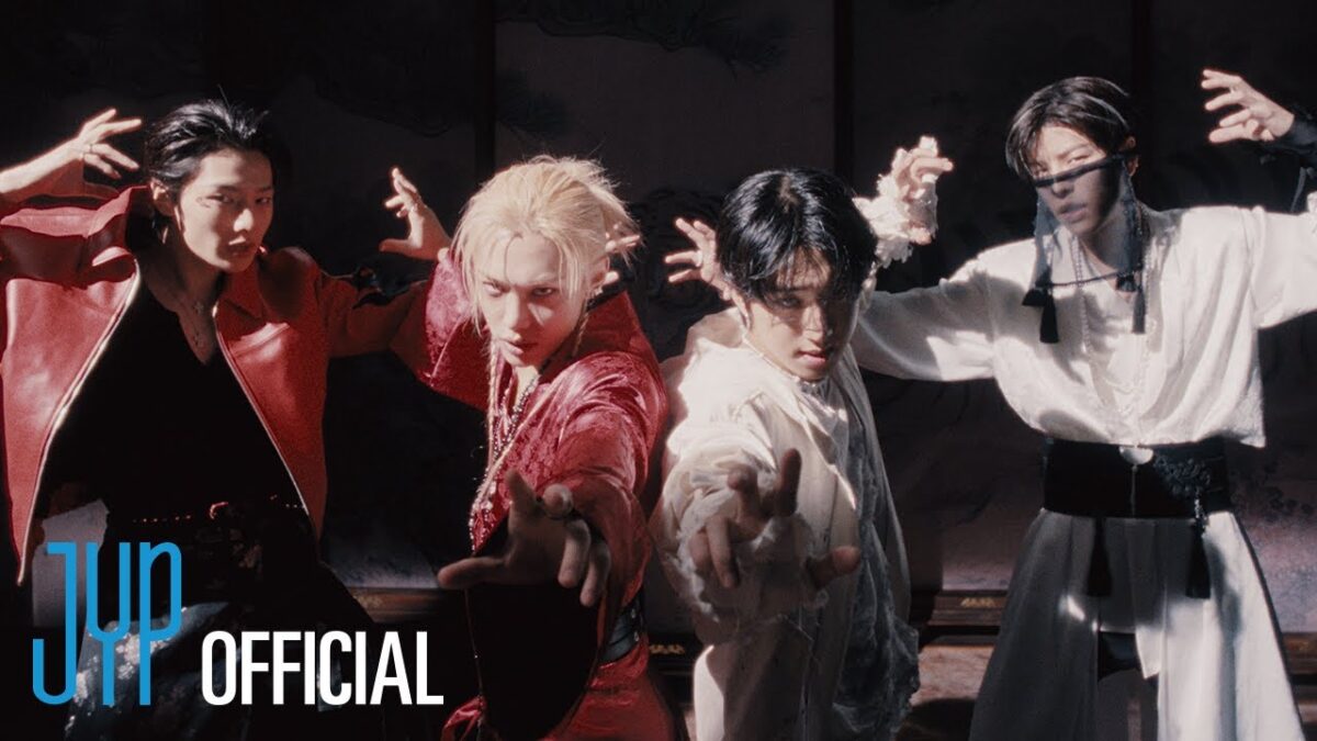 Quatro membros do Stray Kids em poses dramáticas, vestindo trajes coloridos e expressando intensidade no clipe "DIVINE".