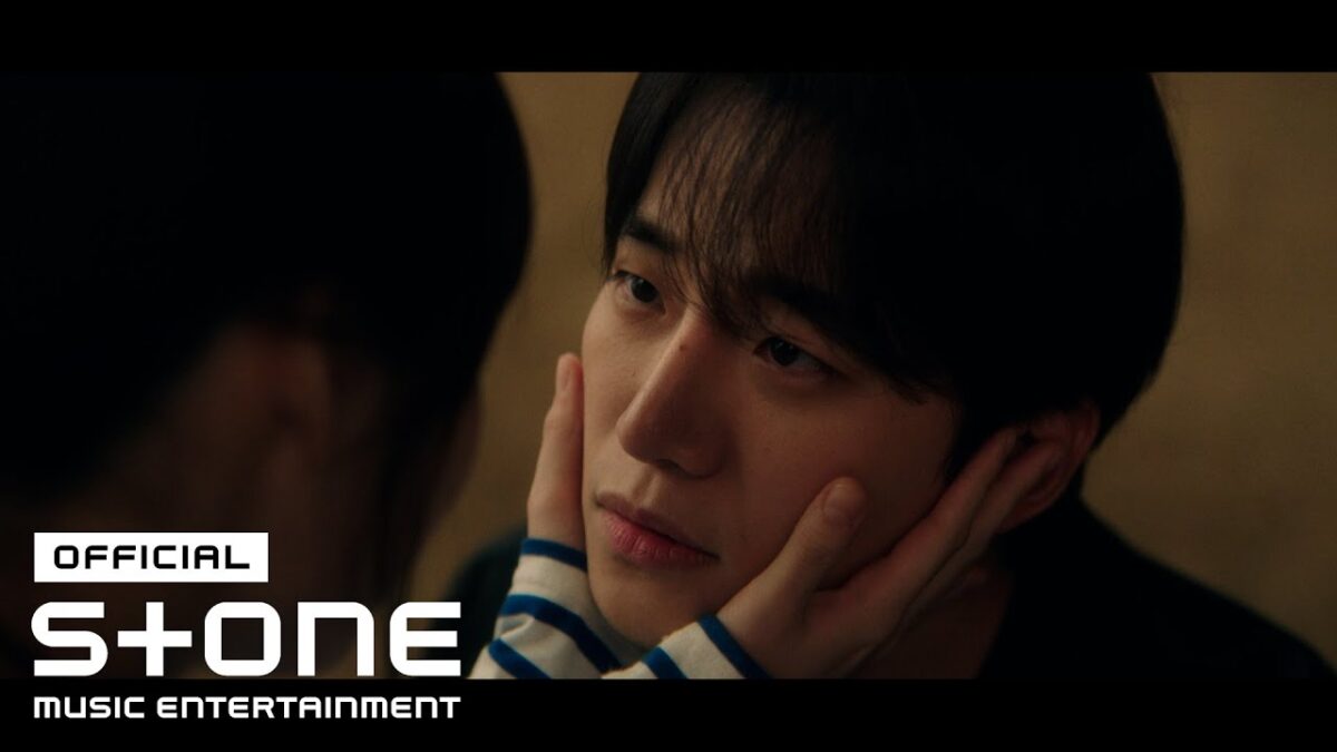 Roy Kim e uma mulher trocando olhares intensos, com ele segurando o rosto dela com delicadeza em ambiente íntimo.