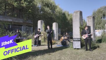 Banda se apresenta ao ar livre com instrumentos em meio a colunas de concreto e vegetação ao fundo.