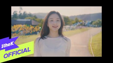 Lee Na Rae sorri enquanto caminha por um caminho em um ambiente ensolarado, com flores ao fundo.
