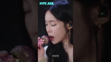Heize canta ao vivo, segurando um microfone decorado enquanto expressa emoção durante a apresentação.