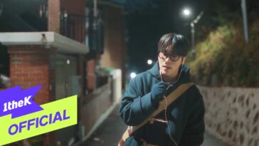 Jovem com óculos e fones de ouvido canta em uma rua tranquila iluminada por postes à noite.