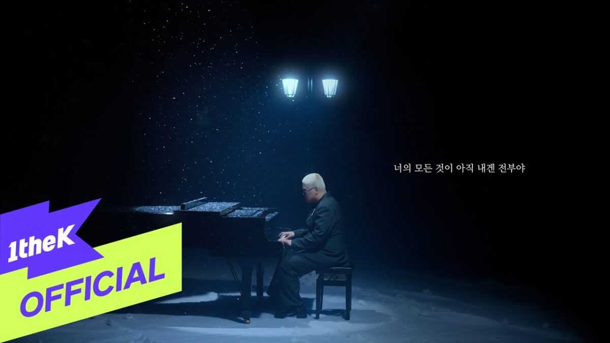 Homem de terno toca piano em um cenário coberto de neve, sob luzes suaves e atmosfera melancólica.