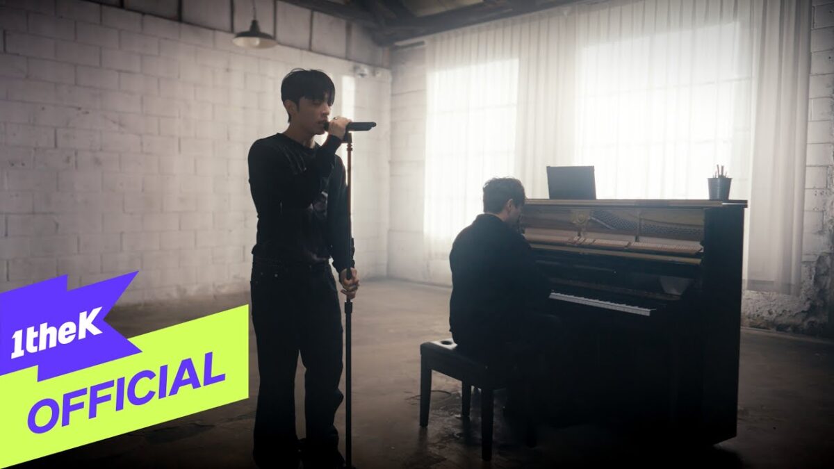 Vocalista da banda First Wish canta em um espaço amplo enquanto um pianista toca ao fundo.