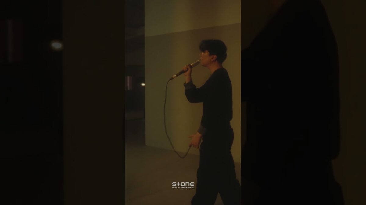 Yoon Hyun Sang se apresenta ao vivo, segurando um microfone em um ambiente iluminado com tons sutis.