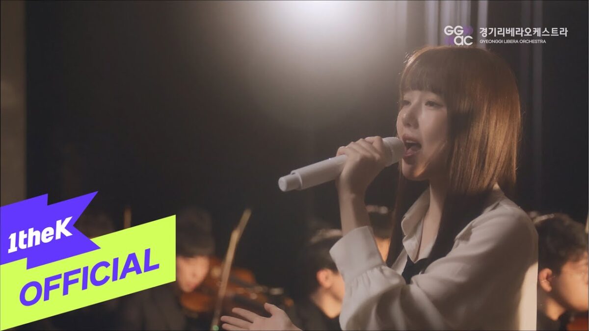 YERIN canta com emoção, acompanhada pela Gyeonggi Libera Orchestra em um ambiente intimista e iluminado.