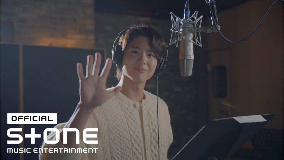 Park Bo Gum sorrindo e acenando enquanto grava em um estúdio de música.