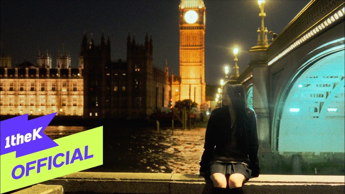 Jovem sentada à beira do rio, com o Big Ben iluminado ao fundo em uma noite clara.