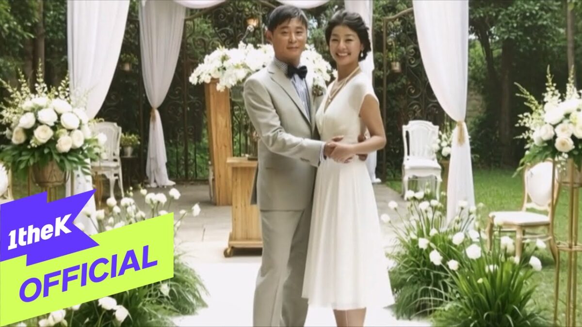 Casal em um cenário romântico, com flores brancas e decoração elegante, sorrindo um para o outro.