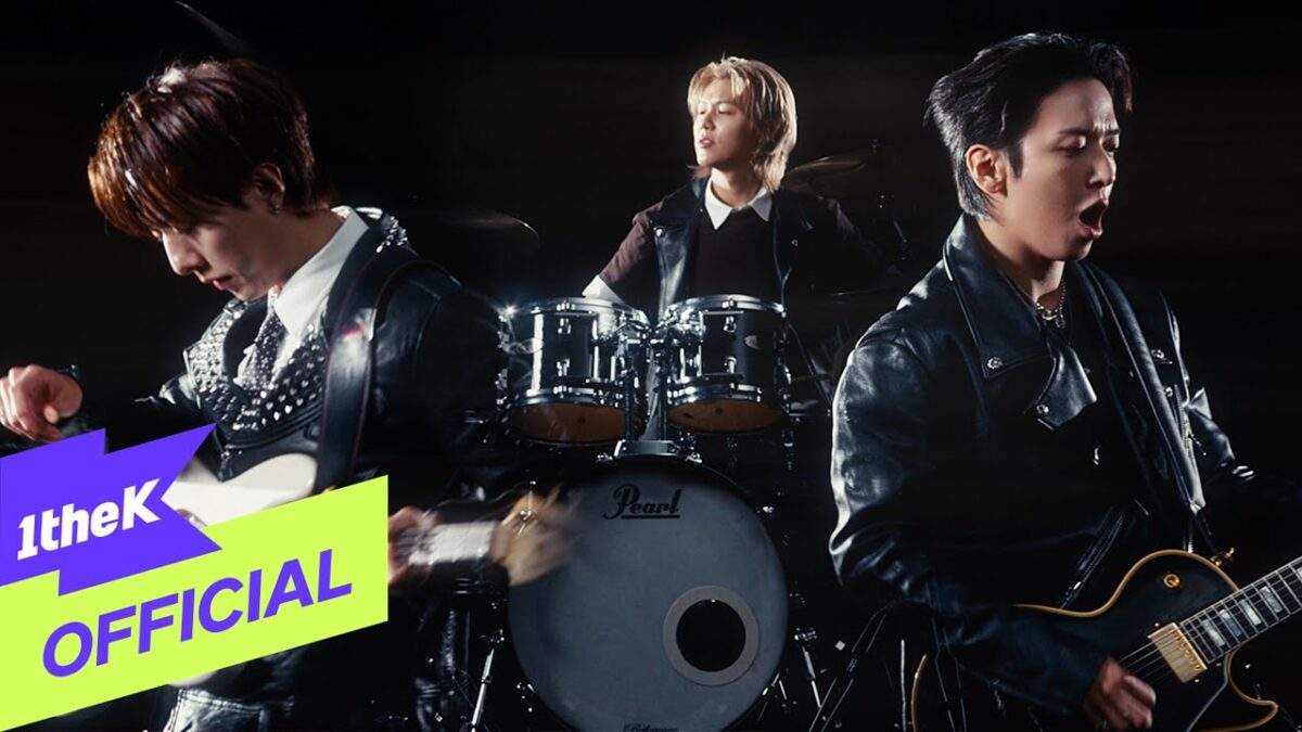 Três integrantes da banda CNBLUE tocam instrumentos em um clipe dinâmico e energético.