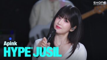 Vocalista da Apink sorri enquanto segura um microfone durante apresentação ao vivo da música "Love Me More".