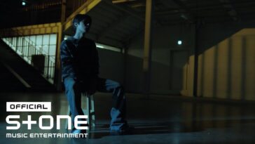 Um jovem sentado em um banco em um ambiente escuro, com luz suave ao fundo.