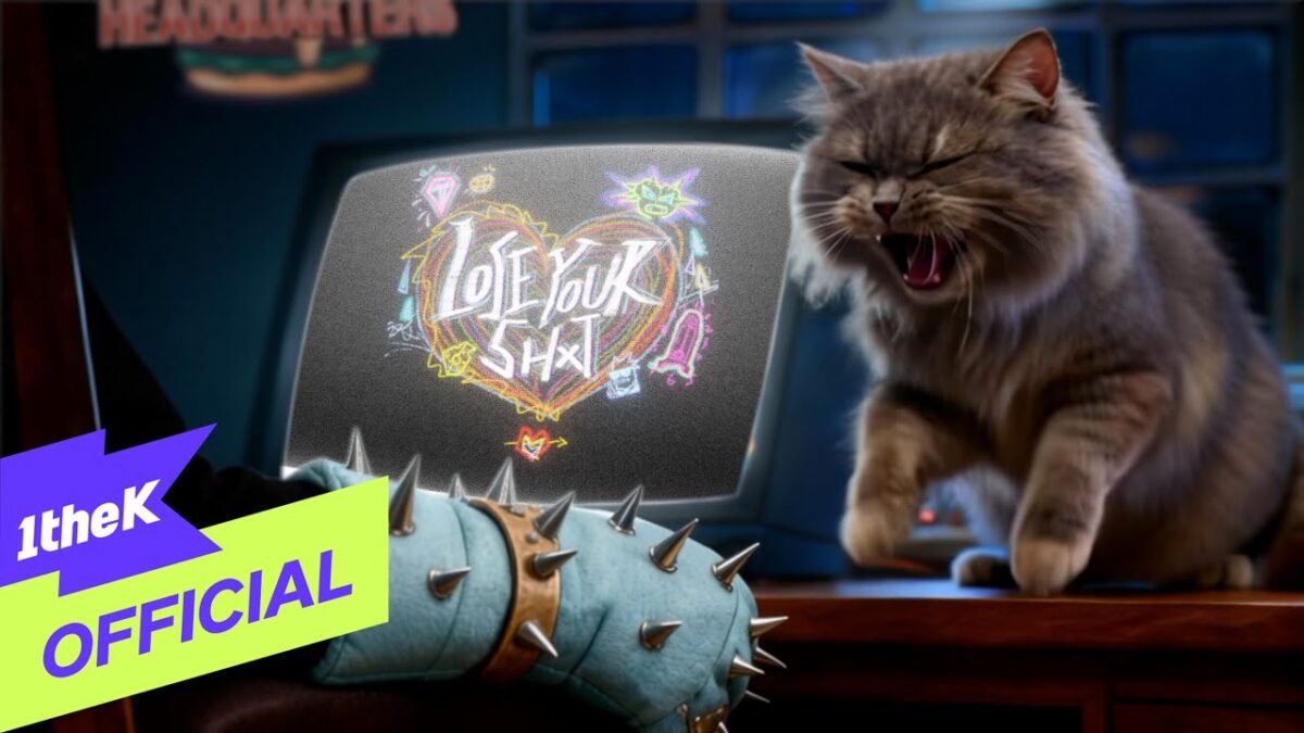 Gato cinza com expressão divertida em frente a um monitor com a frase "Love Your Shit" colorida.