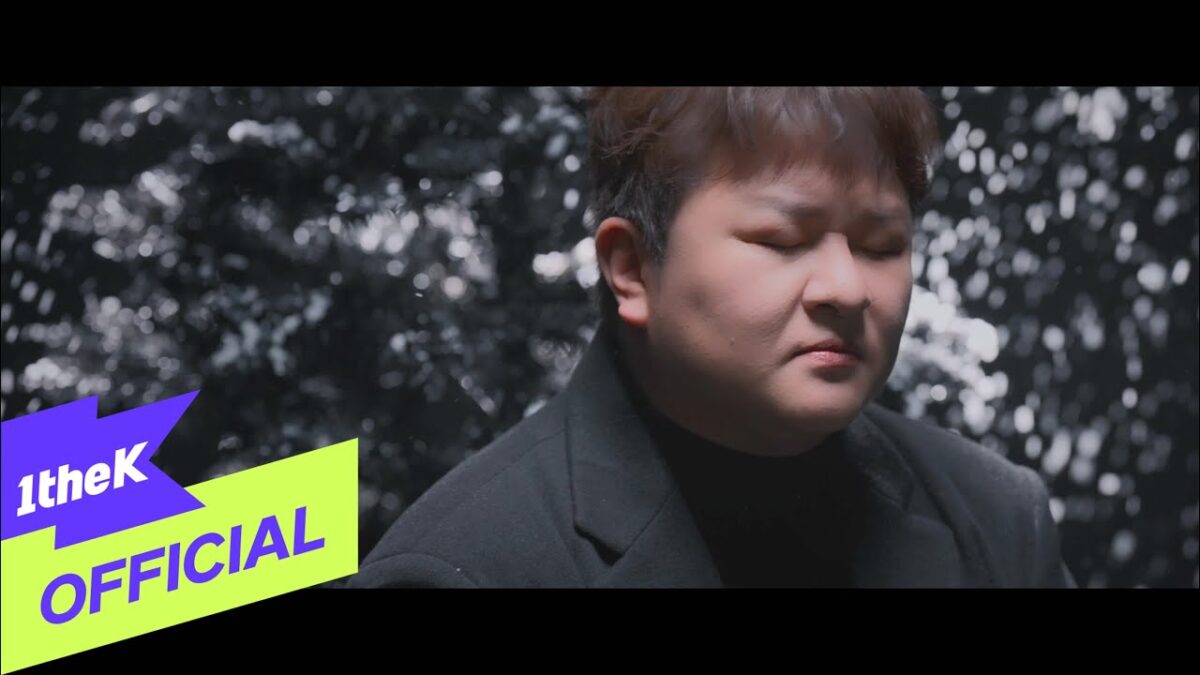 Huh Gak com expressão reflexiva, em meio a um fundo iluminado e suave que evoca a chegada da neve.