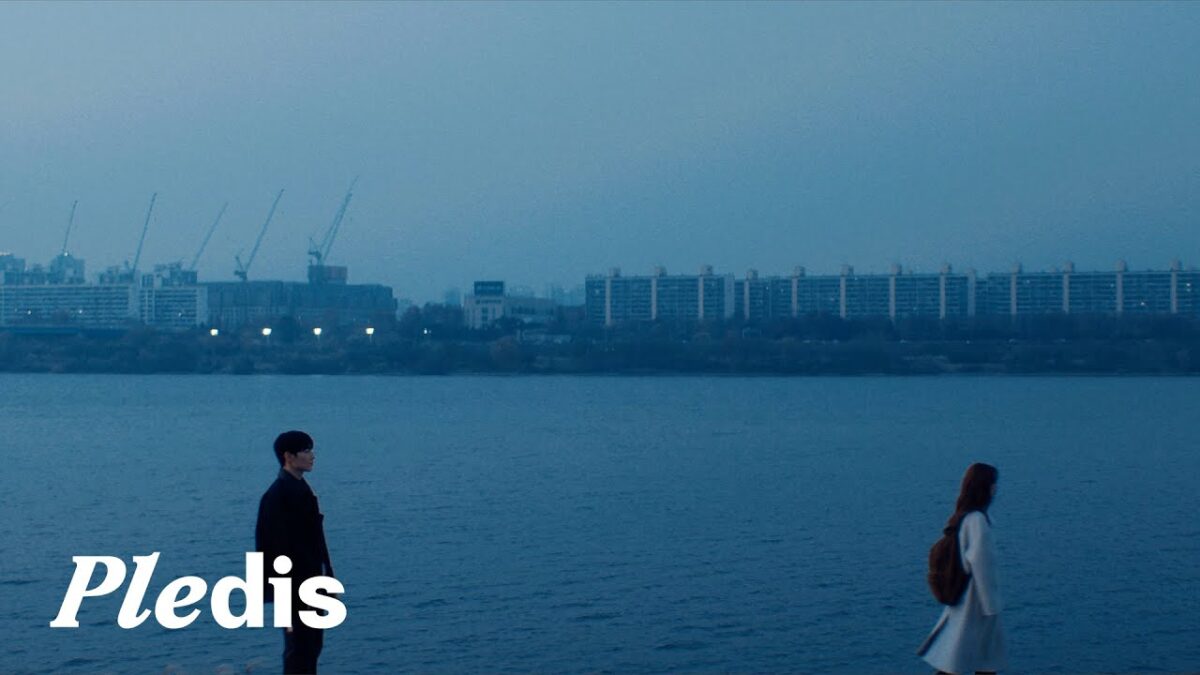 Dokyeom e Seungkwan em um cenário azul à beira do rio, com prédios ao fundo e atmosfera melancólica.