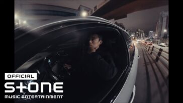 Homem pensativo ao volante de um carro em uma rua iluminada à noite, com prédios ao fundo.