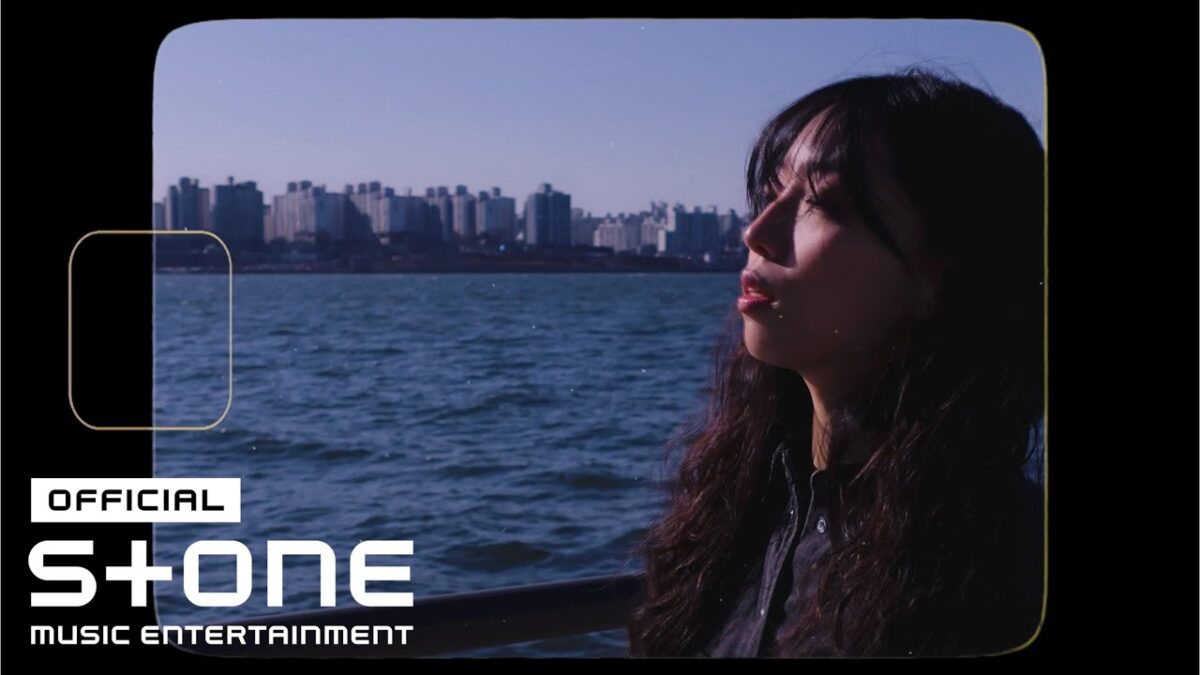 SooYeon observa o horizonte da cidade à beira do rio, em um dia ensolarado.