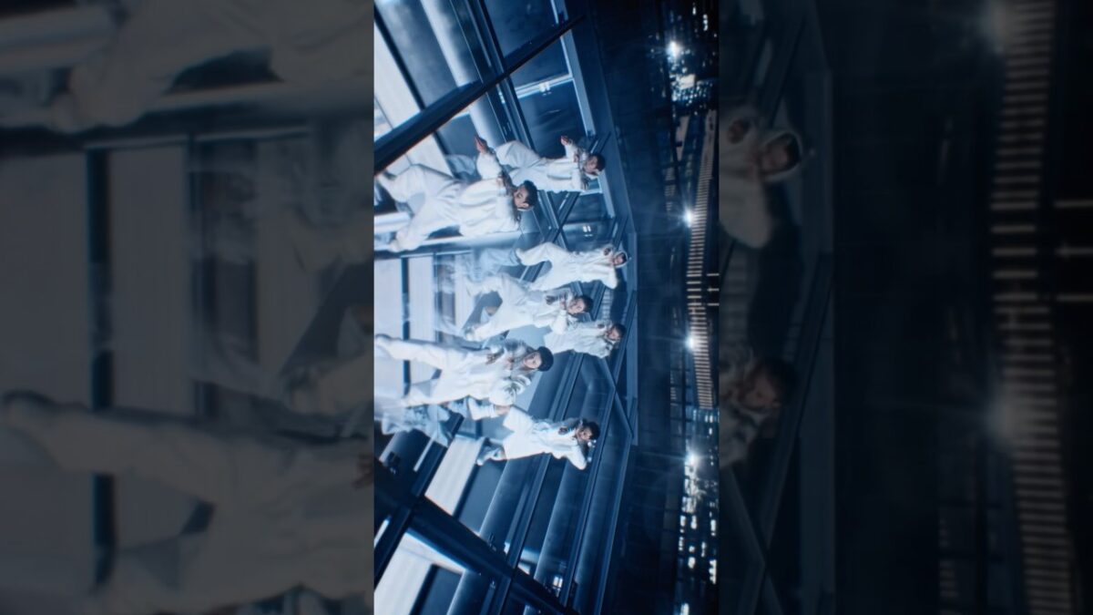 Grupo de dançarinos em trajes brancos, coreografando em um ambiente escuro e futurista com reflexos.