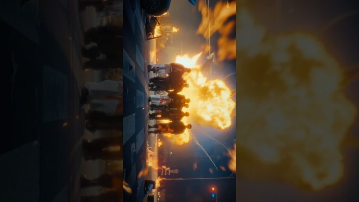 Grupo de pessoas em uma rua, com uma explosão iluminando o fundo e fumaça se espalhando pelo ar.