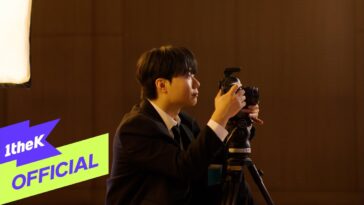 Um jovem em traje formal ajusta uma câmera enquanto se prepara para fotografar em um ambiente iluminado.