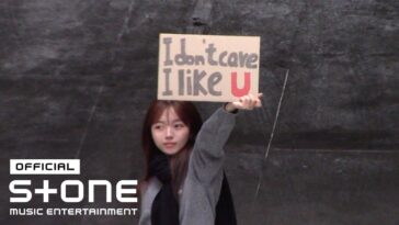 Jovem segura um cartaz escrito "I don't care I like U" em um cenário urbano.