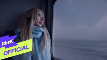 Jovem com cabelo longo e liso, usando fones de ouvido, observa a paisagem pela janela de um trem.