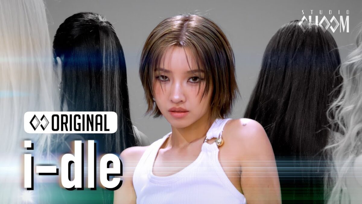 Artista de (G)I-DLE em destaque, com cabelos curtos, em um cenário minimalista e figuras femininas ao fundo.