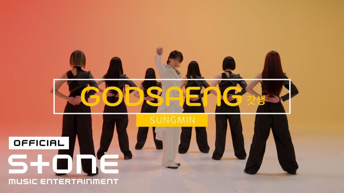 SUNGMIN se destaca em frente a dançarinas em um cenário vibrante, transmitindo energia e movimento.