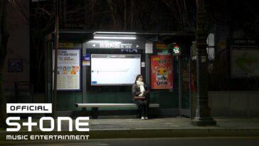 Uma mulher sentada em um ponto de ônibus iluminado à noite, cercada por cartazes e sinalizações.