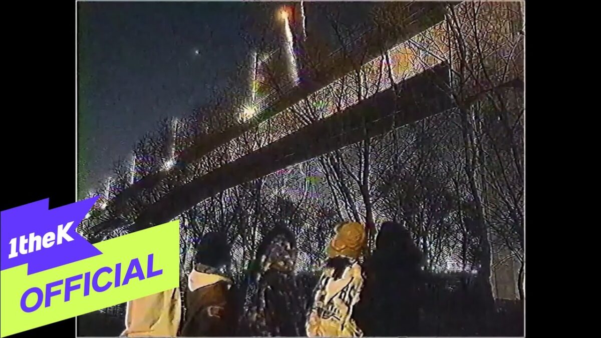 Grupo de pessoas observa fogos de artifício sob uma ponte iluminada em uma noite escura.