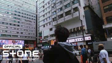 Jovem observa edifícios altos e movimentação de pessoas em uma rua de Hong Kong, com painéis publicitários visíveis.