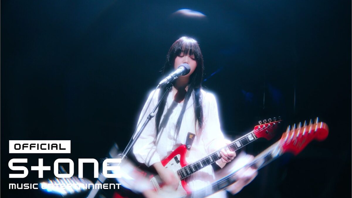 Artista com guitarra em performance ao vivo, iluminada por luzes suaves no palco.