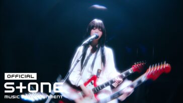 Artista com guitarra em performance ao vivo, iluminada por luzes suaves no palco.