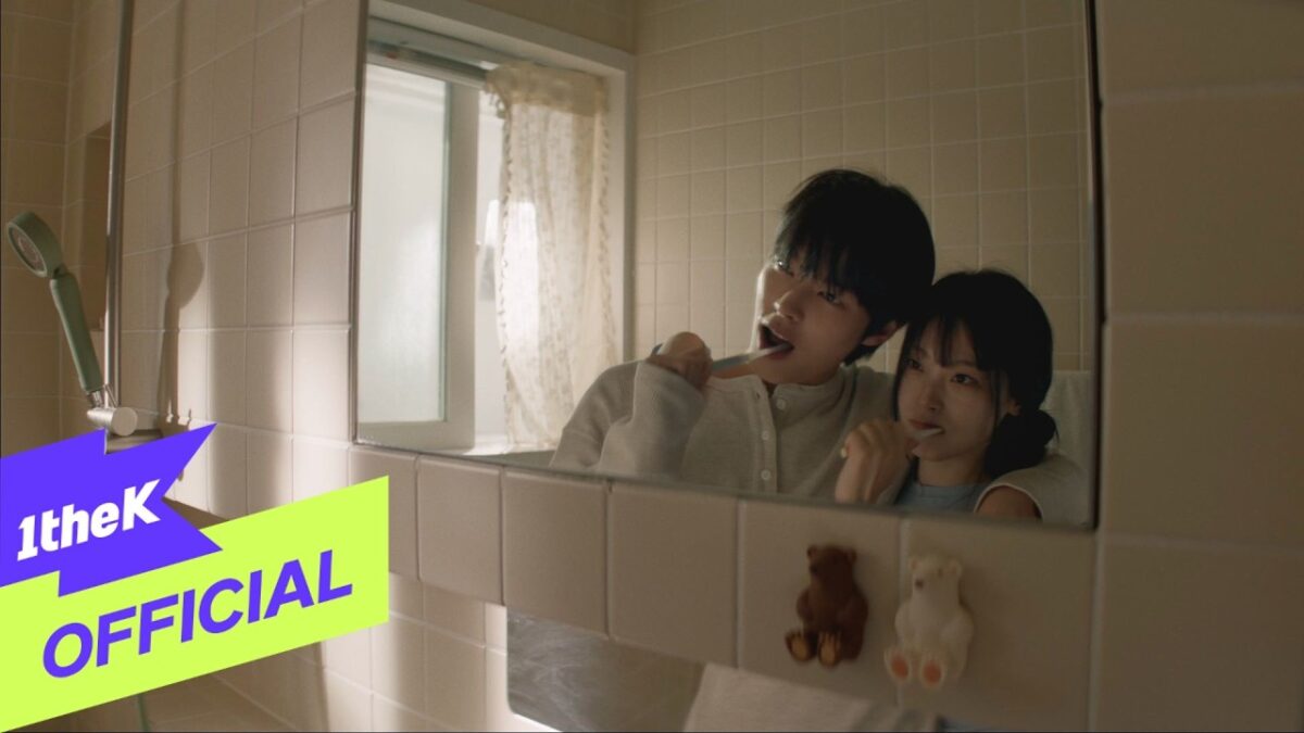 Parc Jae Jung e SULLYOON escovando os dentes juntos em um banheiro com azulejos claros e uma janela ao fundo.