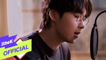Lee Seok Hoon canta em um estúdio, usando óculos, com um microfone próximo ao rosto.