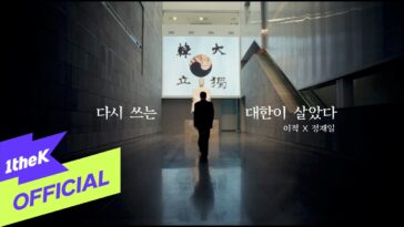 Homem em pé em um corredor amplo, com um mural artístico ao fundo e texto em coreano nas laterais.
