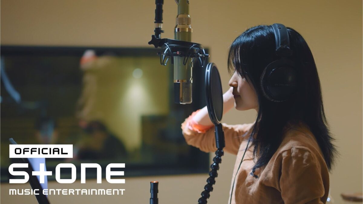 Kim Taeri gravando em estúdio, com fones e microfone, concentrada na performance.