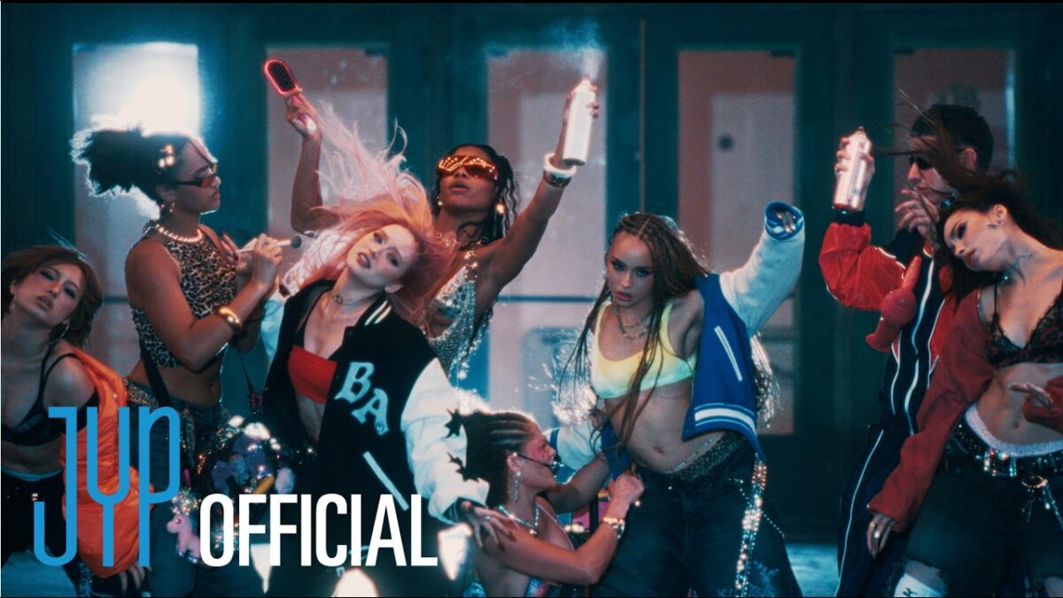 Grupo de mulheres dançando em um videoclipe, com roupas vibrantes e elementos de estilo urbano moderno.