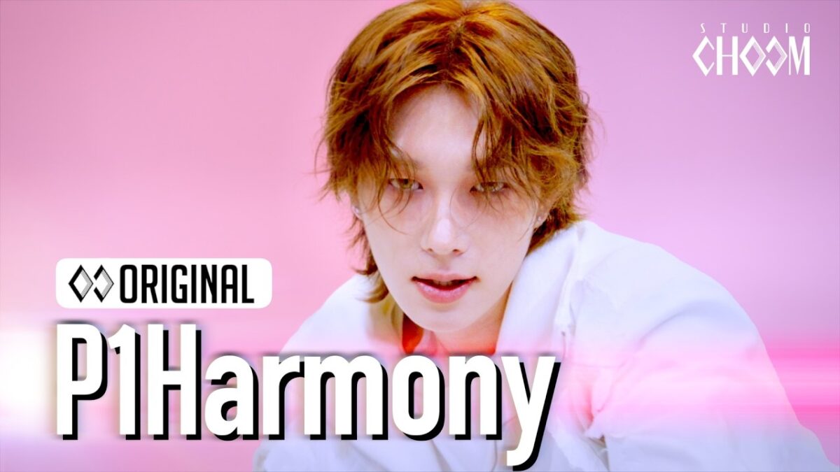 Artista de P1Harmony com cabelo ondulado, olhando intensamente para a câmera em fundo rosa.