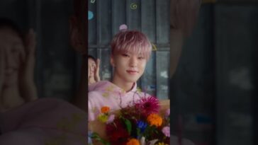 HOSHI sorri enquanto segura um buquê colorido de flores em um ambiente alegre.