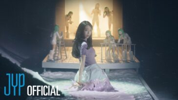 Yuna em um cenário vibrante, cercada por bonecas com cabelo verde, em uma performance cheia de energia.
