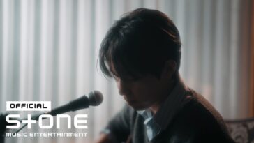 BUMJIN, em um ambiente suave, toca violão enquanto olha para baixo, transmitindo emoção em seu clipe musical.