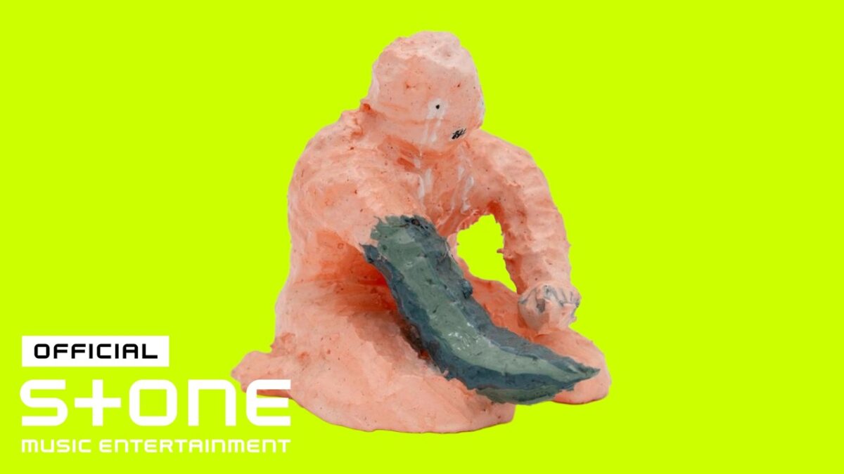 Escultura de personagem em tons de rosa, segurando uma lâmina, sobre fundo amarelo vibrante.